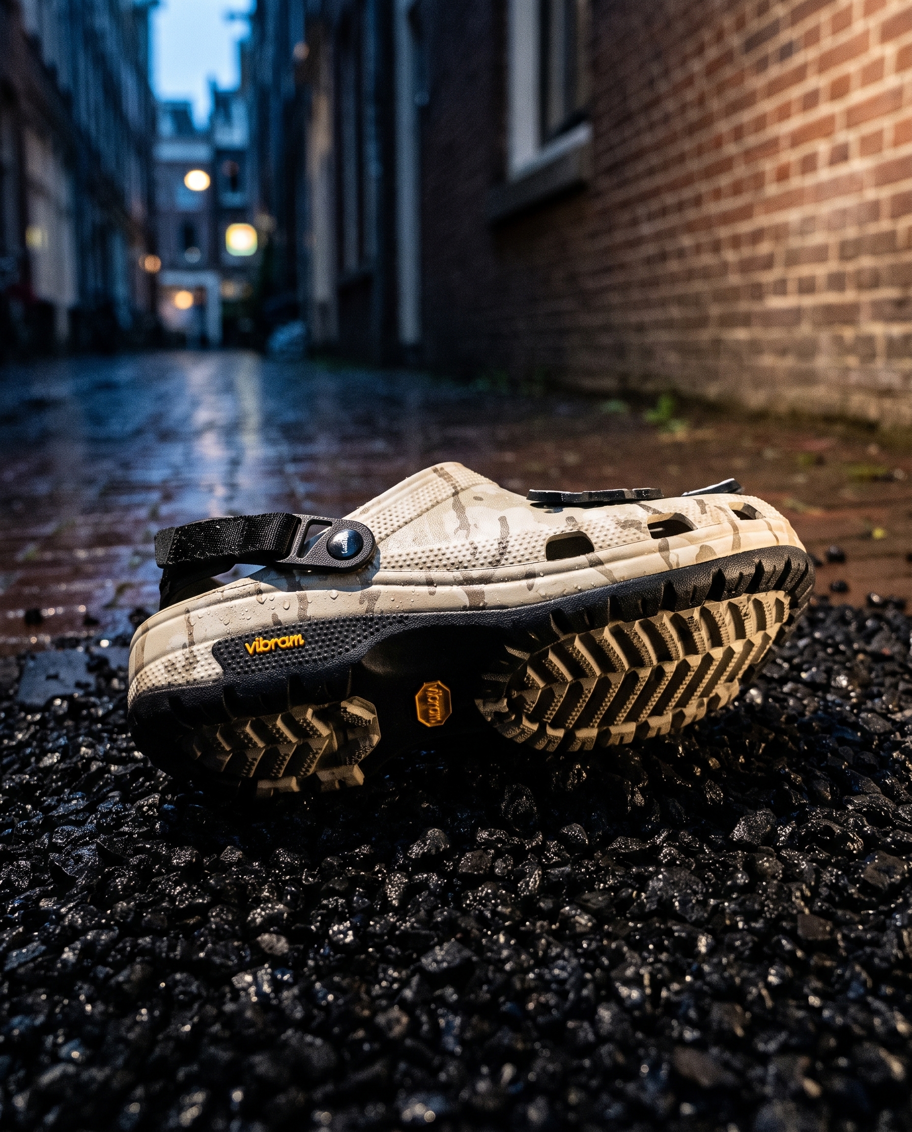 A rugged foam clog with a lugged outsole on wet black gravel at blue hour